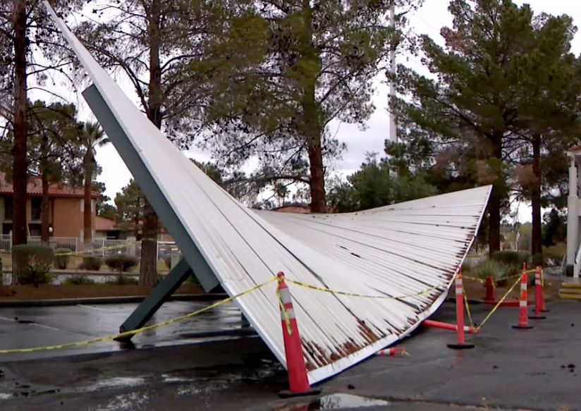 A failed budget fabric carport collapsed across a parking lot, taped off with cones